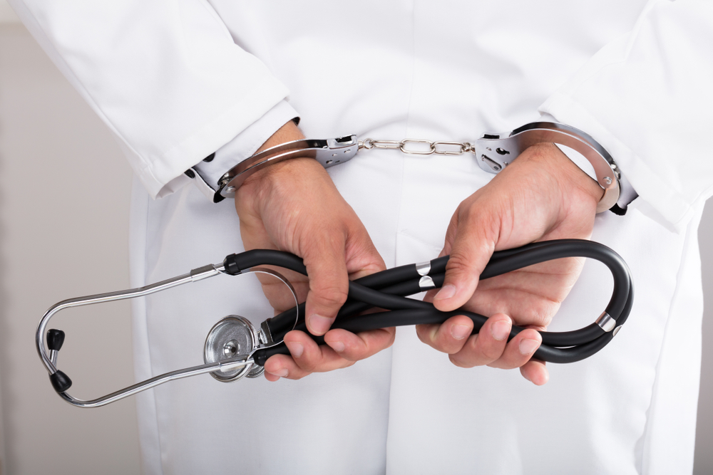 Doctor's Hand with Handcuff Holding Stethoscope Behind Photo of Doctor's Hand with Handcuff Holding Stethoscope Behind